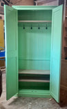 A green hallway storage cupboard with coat hooks and three shelves, made from pine wood, with its two doors open.