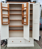 A large white storage cabinet with two open doors, showing multiple wooden shelves inside. The cabinet has two drawers at the bottom with round wooden knobs 
