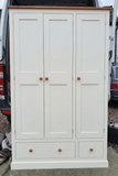 white three-door kitchen larder cupboard with doors closed, a natural wood top and two lower drawers.