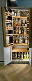 A 2-door cocktail/drinks cabinet with storage racks, filled with various bottles and shakers. The cabinet has a light wood finish and is open, revealing the interior shelving.