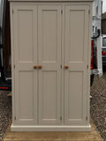 A traditional style solid pine wood storage cupboard withthree doors and a flat top, featuring wooden knobs and multiple internal shelves.