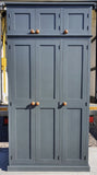 A traditional style solid pine wood storage cupboard withthree doors and a flat top, featuring wooden knobs and multiple internal shelves.