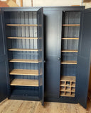 A large blue kitchen larder cupboard with double doors, featuring an integrated wine rack and multiple shelves made of contrast wood, designed to hold wine and spices.