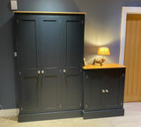 A 3-door coat storage cupboard with shaker doors and a small 2-door shoe storage cupboard with sloping shelves, placed against a dark wall with a lamp and a decorative object on top of the shoe storage unit.