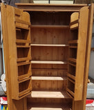 A large kitchen larder pantry cabinet with open doors, displaying wooden interior shelves, in a waxed finish.